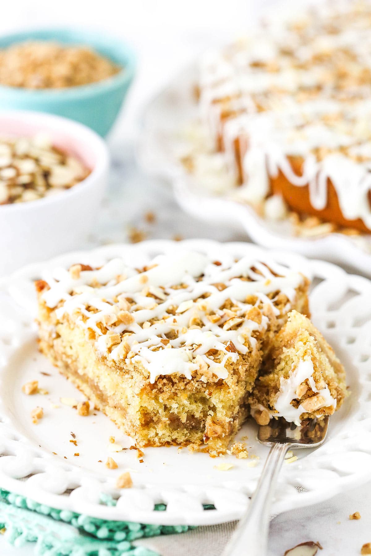 A piece of toffee almond coffee cake on a plate with one bite on a metal fork