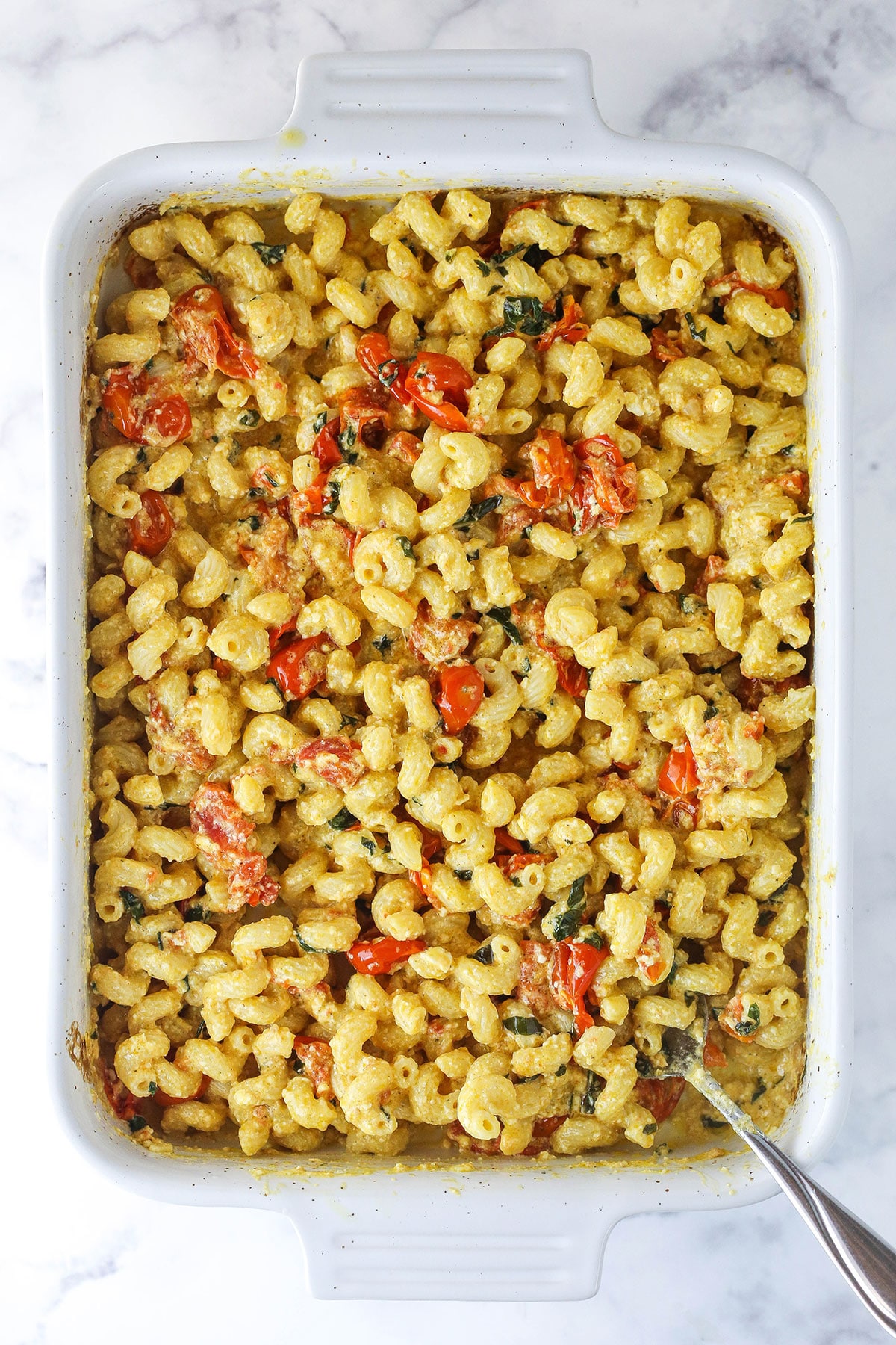 A baking dish full of freshly made baked feta pasta with a metal spoon in the corner