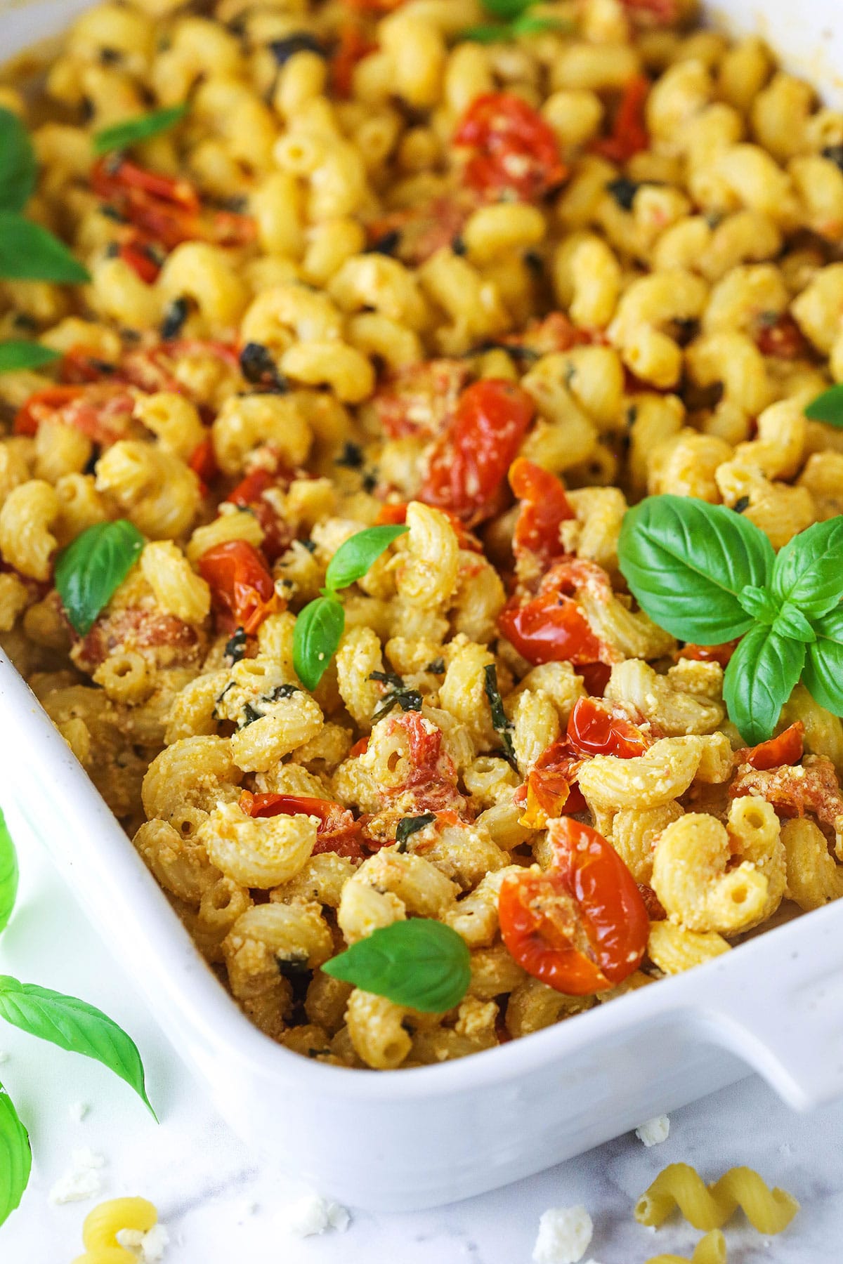 A close-up shot of a pasta casserole with tomatoes, basil and feta cheese in a baking dish