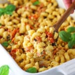 A wooden spoon scooping out a spoonful of baked feta pasta from a white baking dish