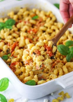 A wooden spoon scooping out a spoonful of baked feta pasta from a white baking dish