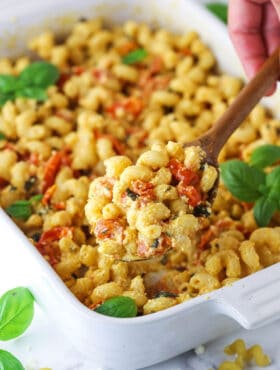 A wooden spoon scooping out a spoonful of baked feta pasta from a white baking dish