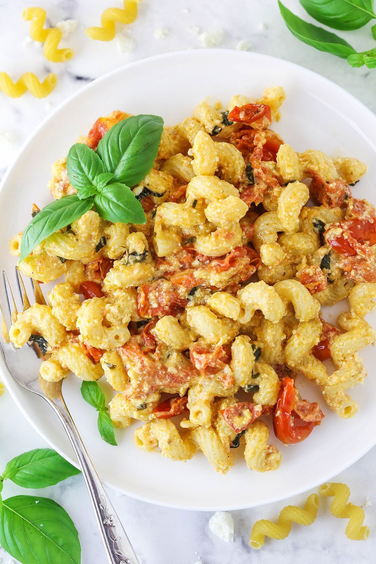 A white plate full of baked feta pasta with a cluster of basil leaves as a garnish