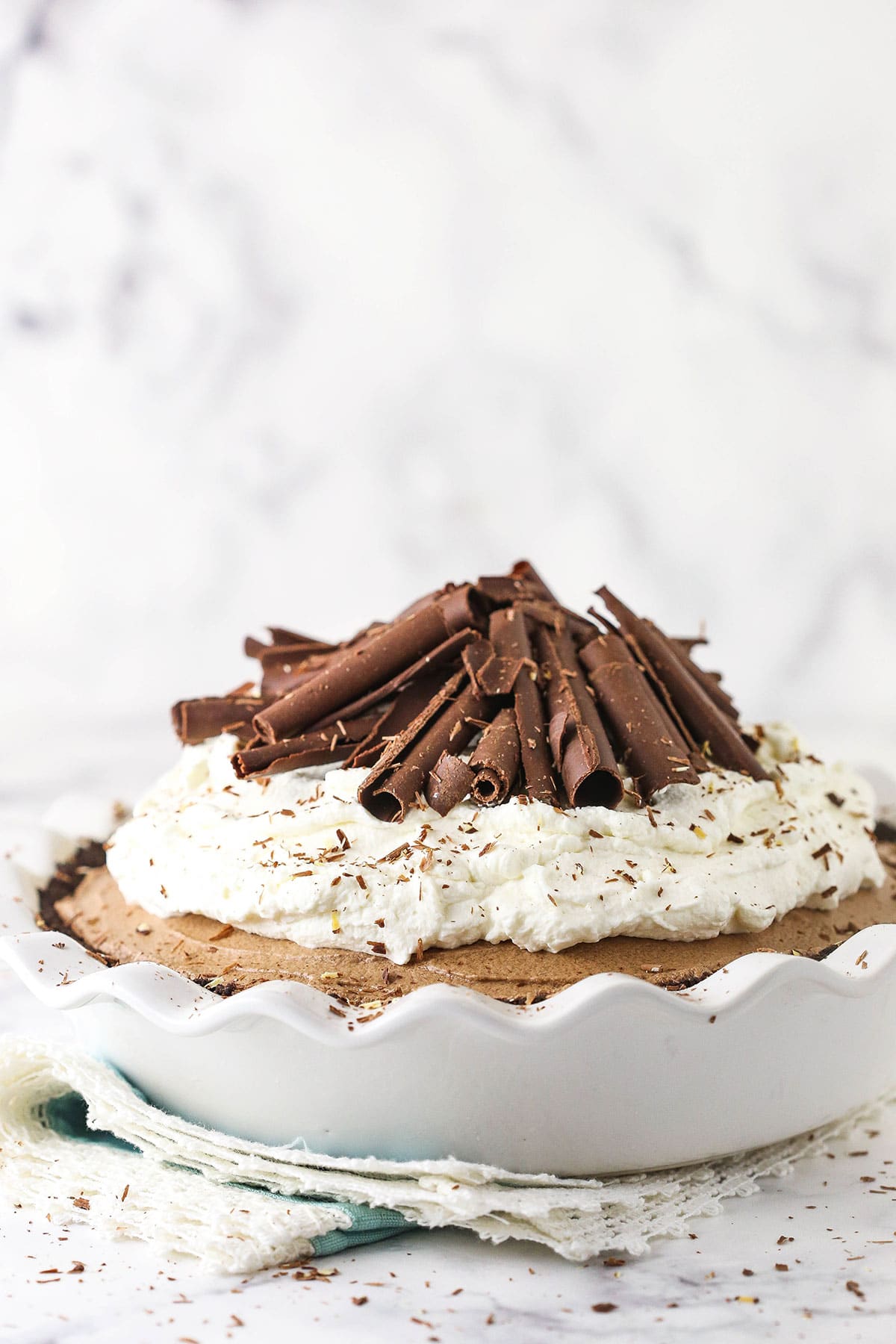 french silk pie in white pie dish with whipped cream and chocolate curls on top