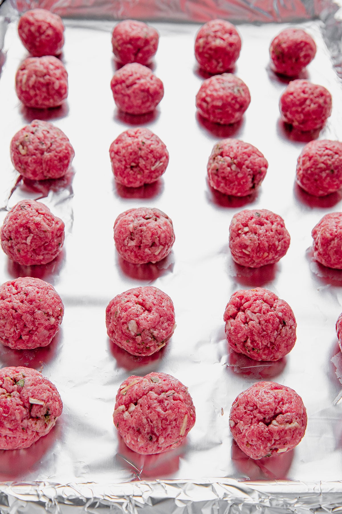 Uncooked meatballs lined up on a baking sheet covered in aluminum foil