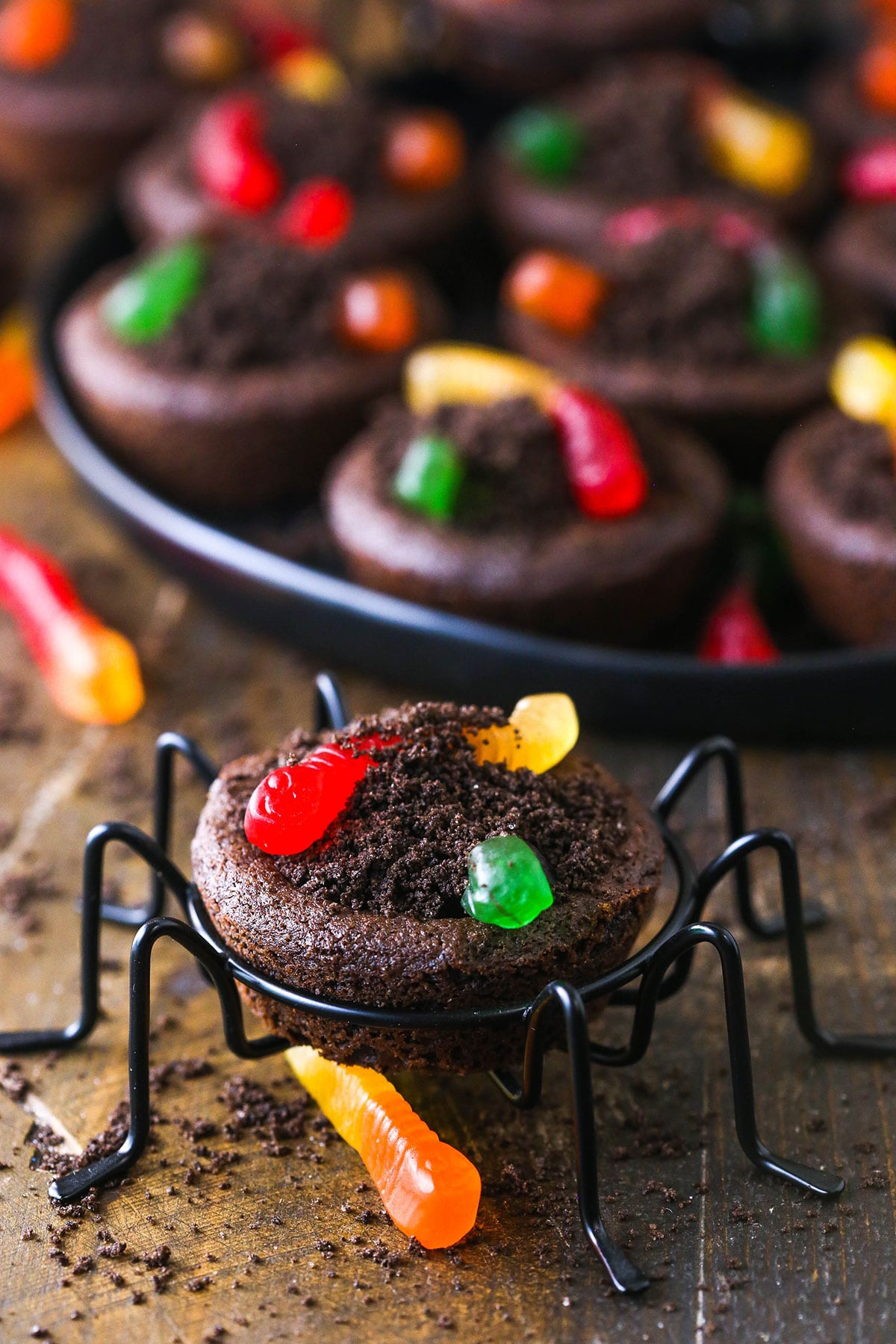 A dirt cookie cup on a small spider stand with a tray full of cookies in the background