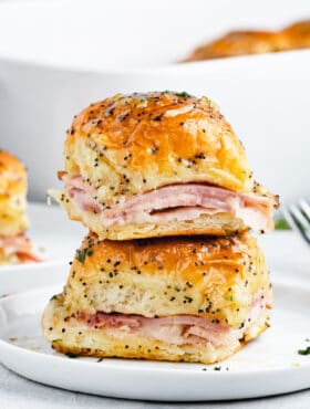 Two ham and cheese sliders stacked on top of one another on a plate