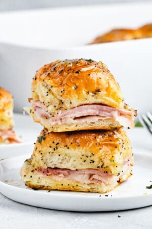 Two ham and cheese sliders stacked on top of one another on a plate