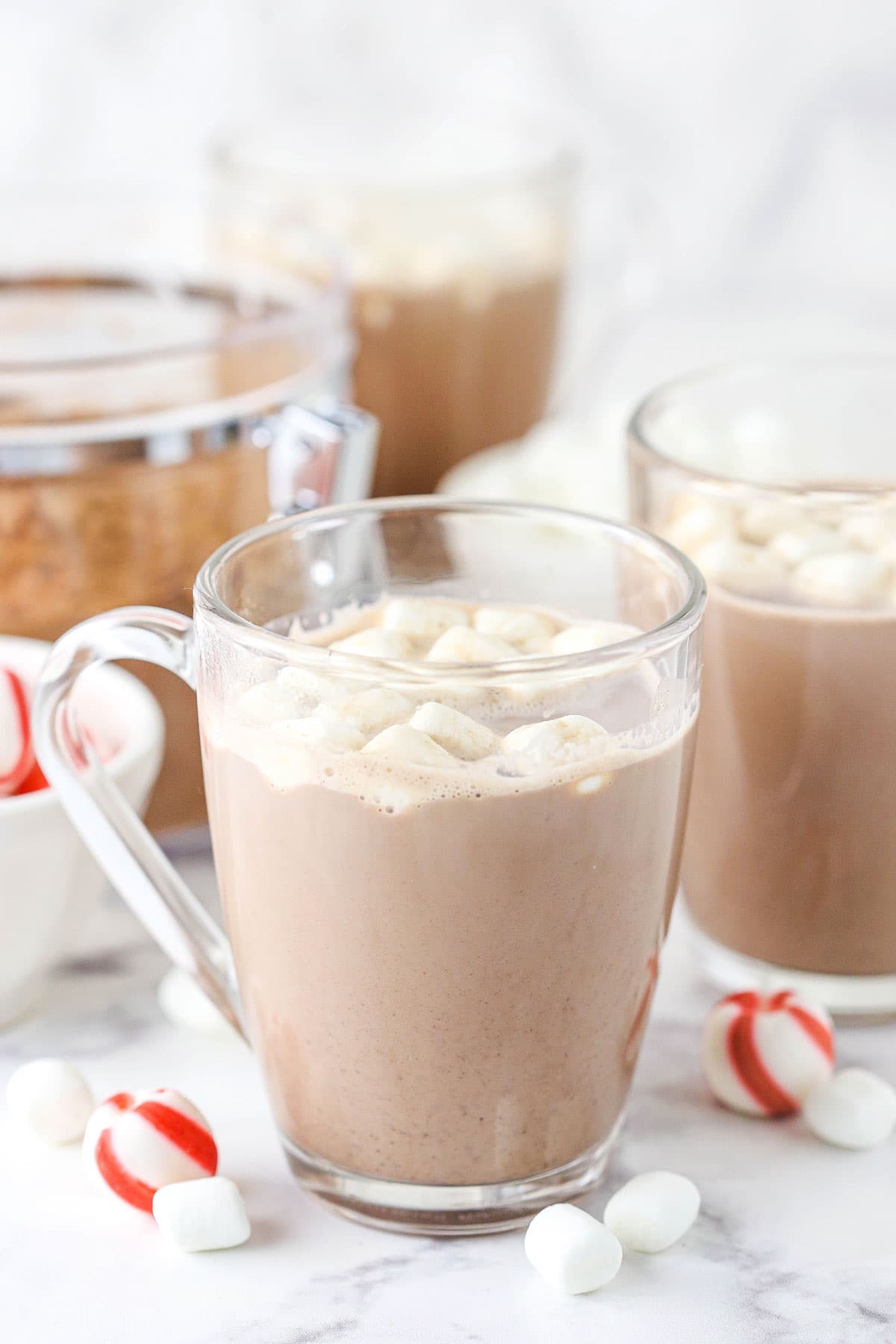 A cup of hot chocolate on a marble counter with peppermints and mini marshmallows