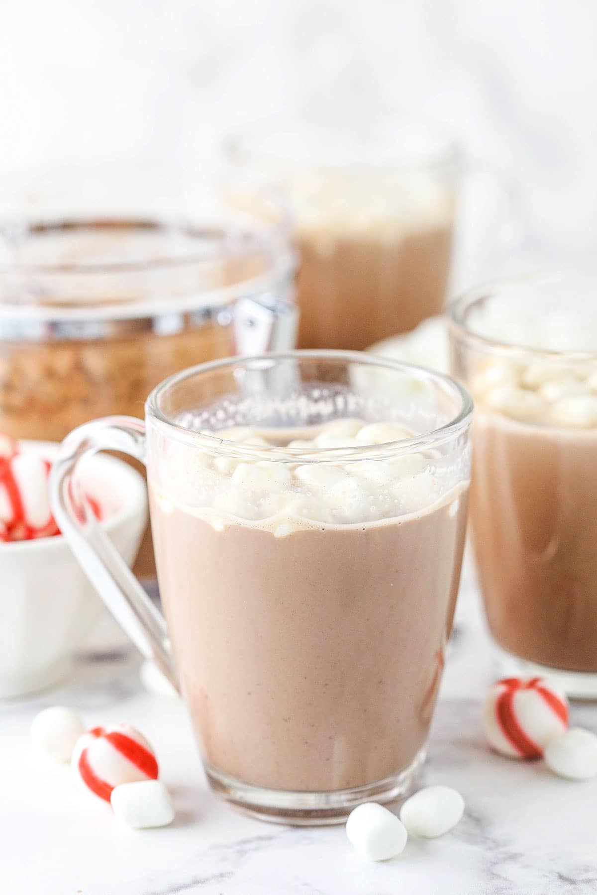 A glass mug full of homemade hot cocoa with peppermint candies in a bowl beside it