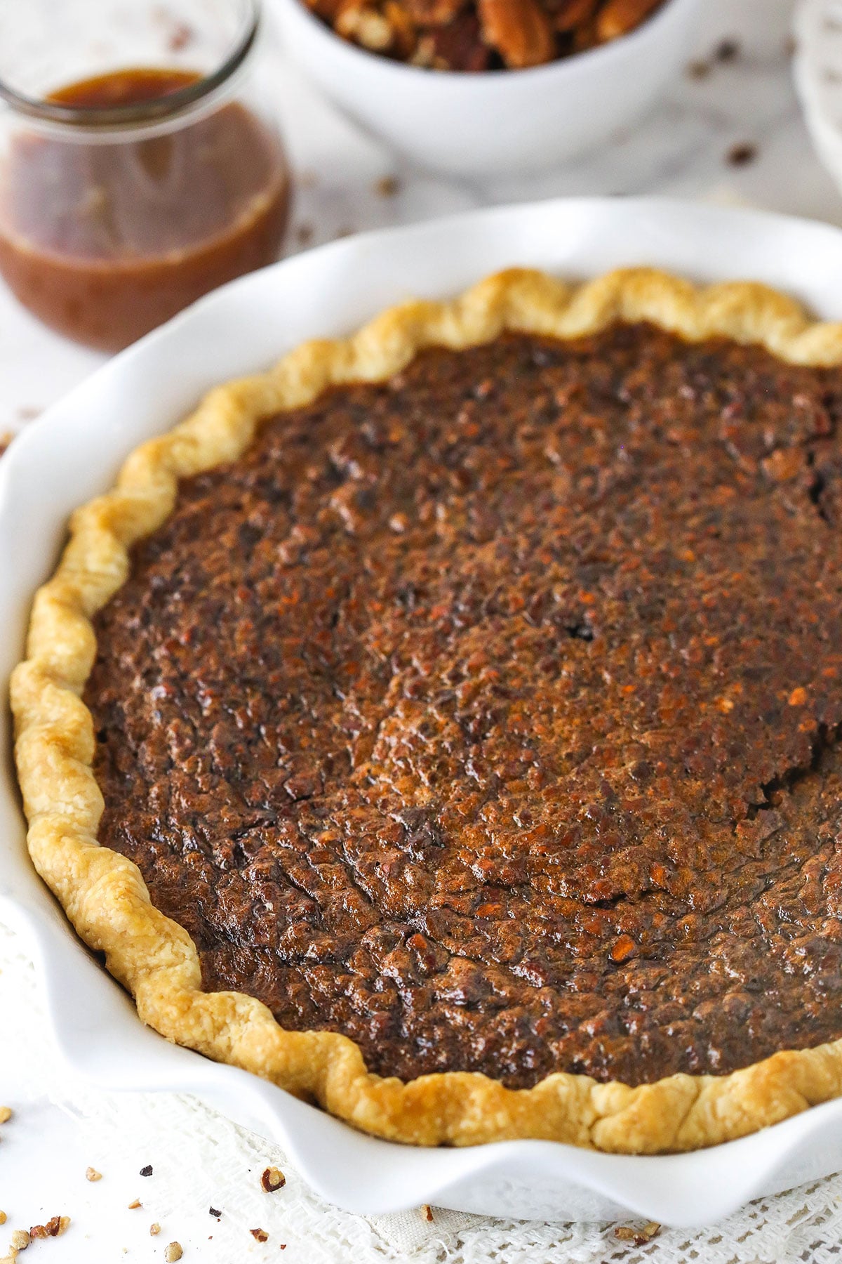 A caramel pie in a white pie dish beside a glass full of caramel sauce