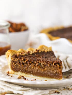 A slice of pie on a plate with a jar of caramel sauce and more pie in the background