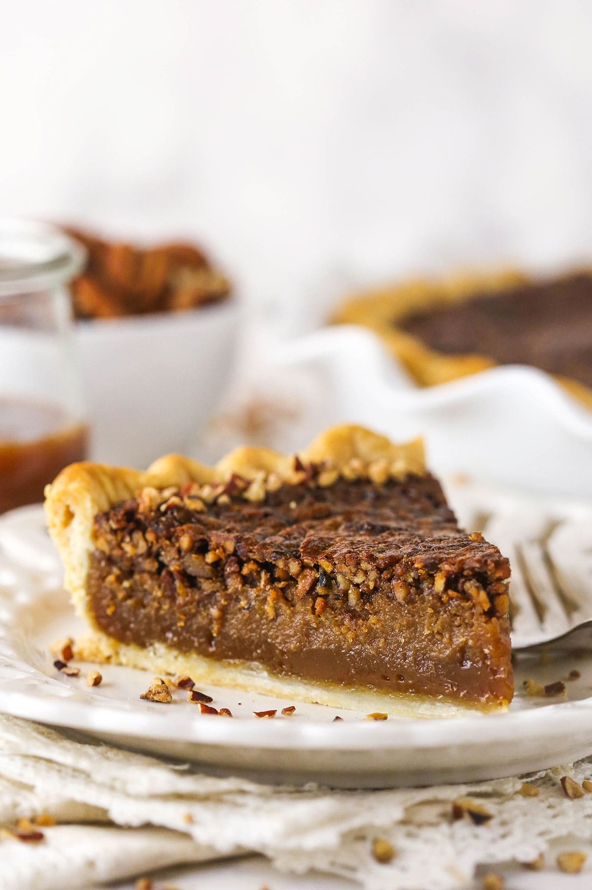 A slice of pie on a plate with a jar of caramel sauce and more pie in the background