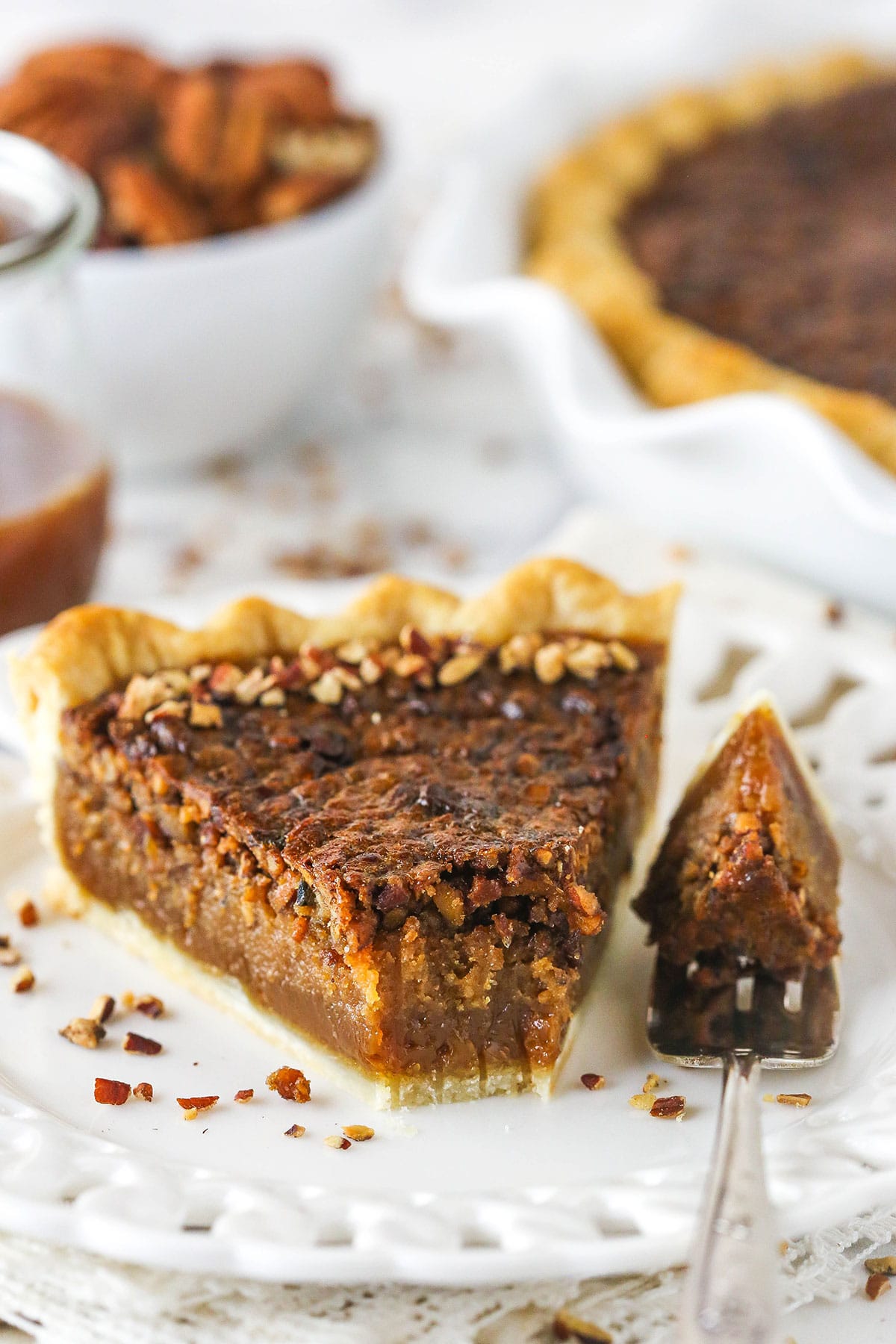 A slice of caramel pecan pie on a plate with one bite on a metal fork