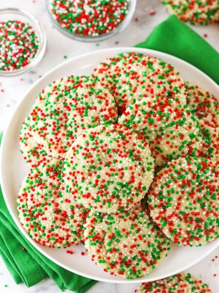 A plate piled high with sugar cookies coated in red, white and green nonpareil sprinkles