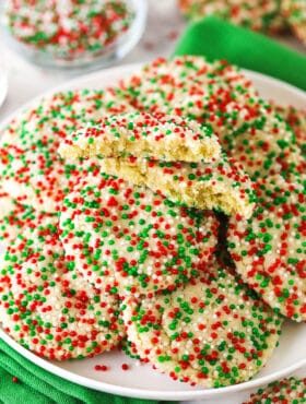 Christmas sprinkle cookies piled onto a white plate with one broken in half to reveal the soft and fluffy interior