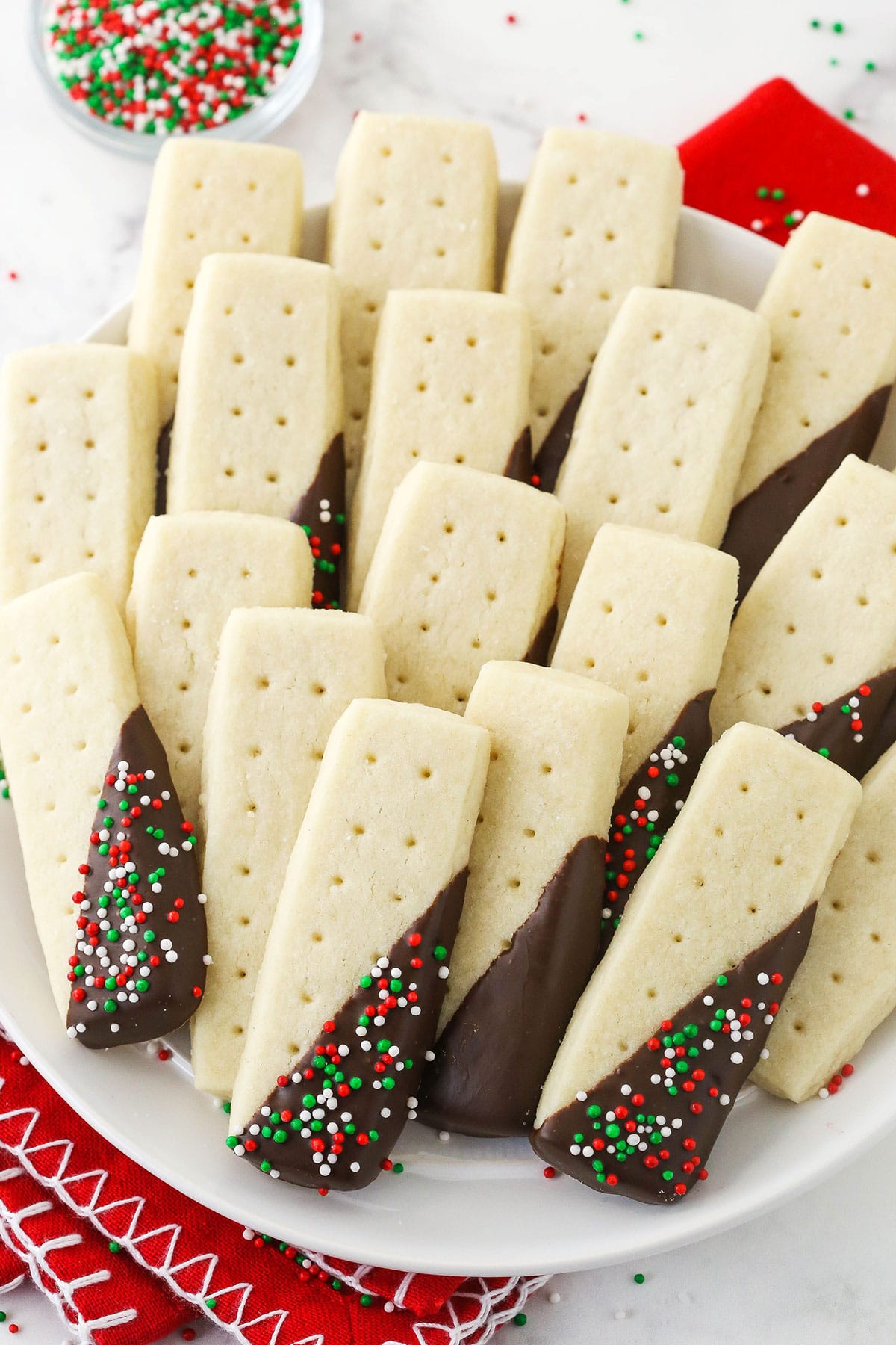 A platter full of rectangular shortbread cookies with some dipped in chocolate and others plain.