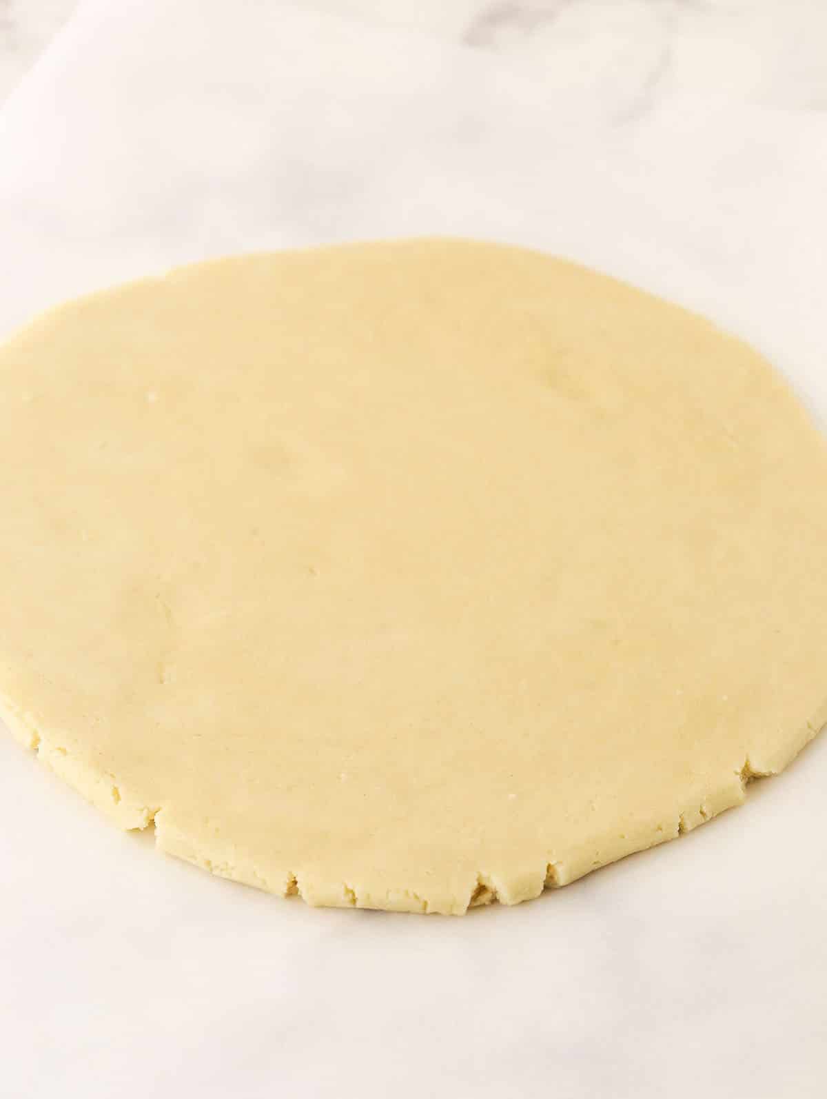 A disc of rolled out shortbread dough on top of a white surface.