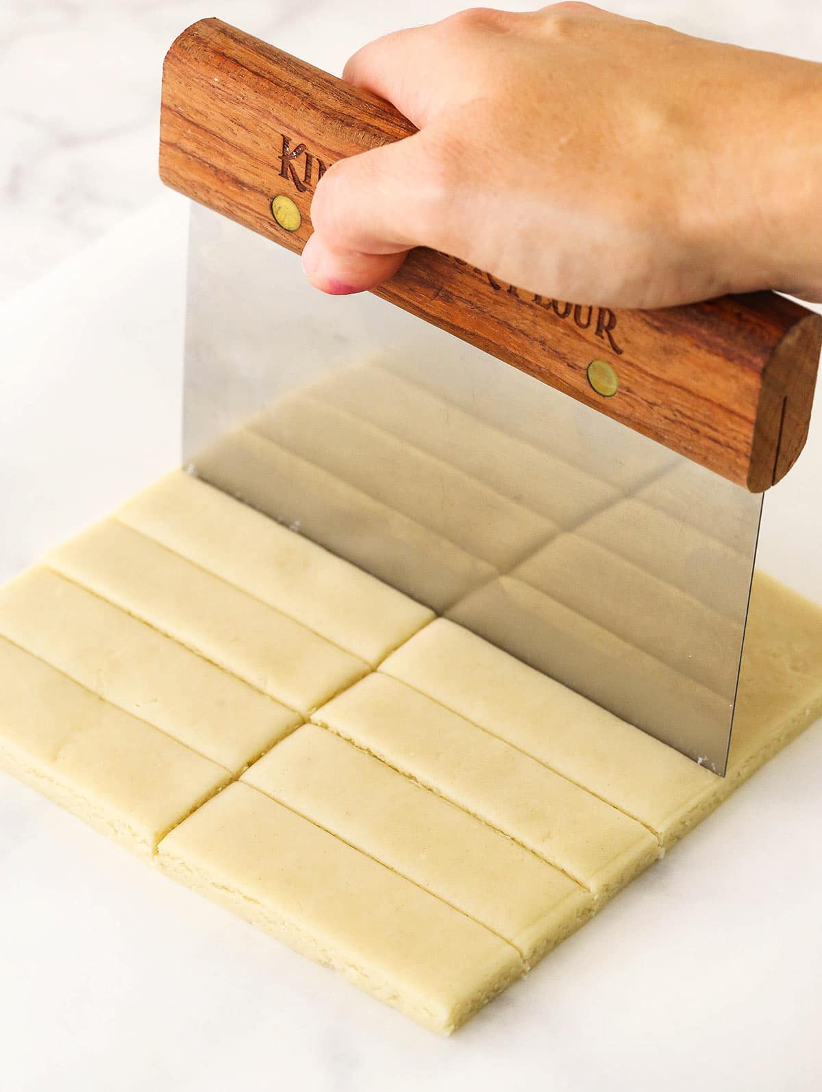 A pastry cutter slicing out rectangle shapes from the slab of cookie dough.