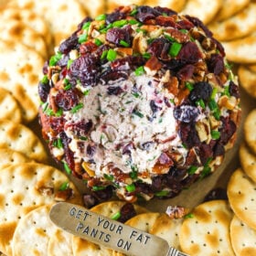 A cheeseball with a chunk removed beside a spreader carved with the words "get your fat pants on"