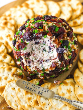 A cheeseball with a chunk removed beside a spreader carved with the words "get your fat pants on"