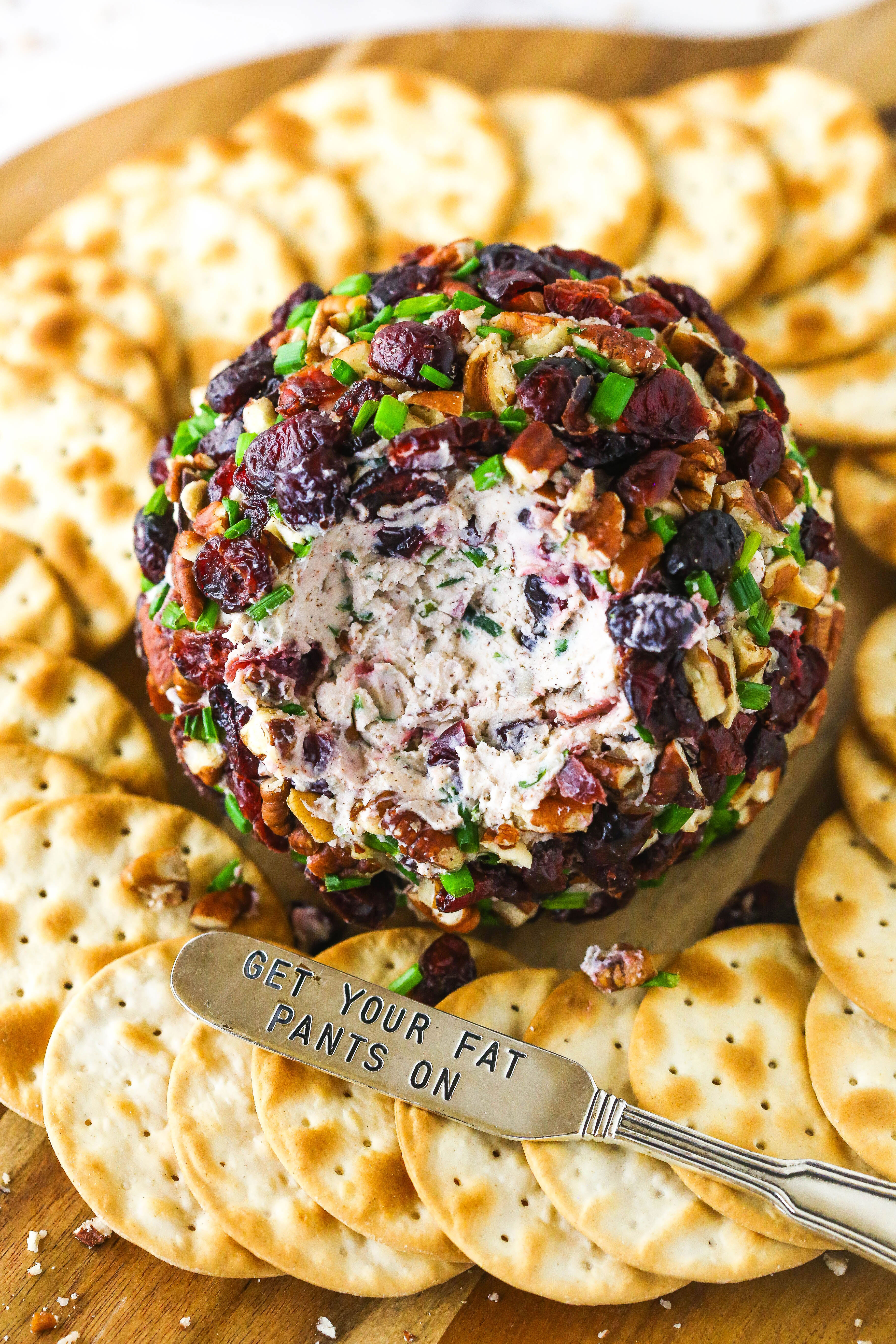 A cheeseball with a chunk removed beside a spreader carved with the words "get your fat pants on"