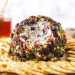 A cranberry pecan cheeseball on a wooden cutting board with a cup of cranberry juice in the background