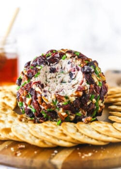 A cranberry pecan cheeseball on a wooden cutting board with a cup of cranberry juice in the background