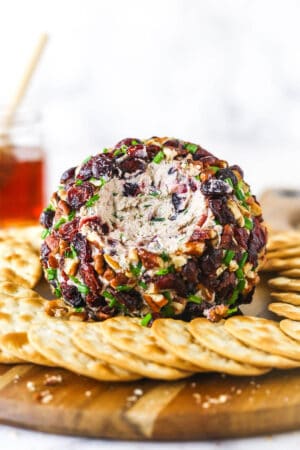 A cranberry pecan cheeseball on a wooden cutting board with a cup of cranberry juice in the background