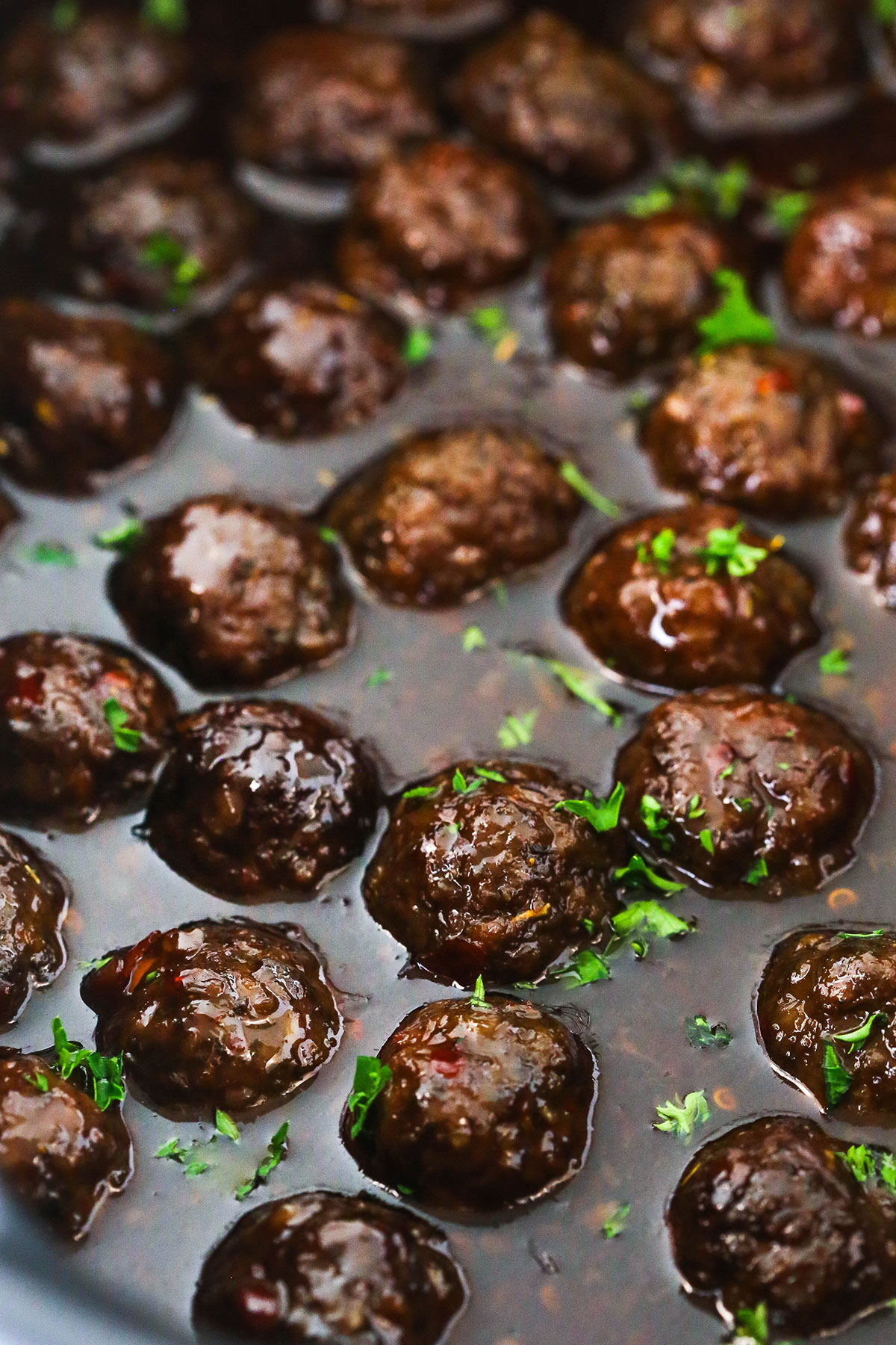grape jelly meatballs with parsley partially submerged in sauce in crockpot
