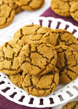 A pile of crackly gingersnaps on a plate sitting on top of a folded kitchen towel