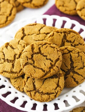 A pile of crackly gingersnaps on a plate sitting on top of a folded kitchen towel