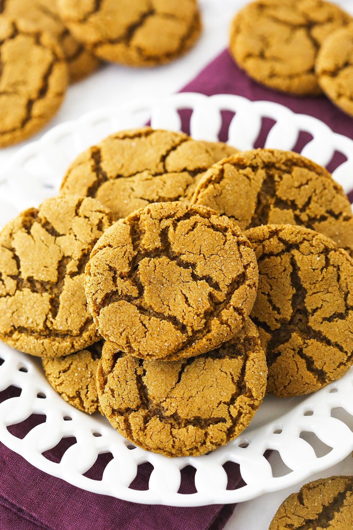 A pile of crackly gingersnaps on a plate sitting on top of a folded kitchen towel.