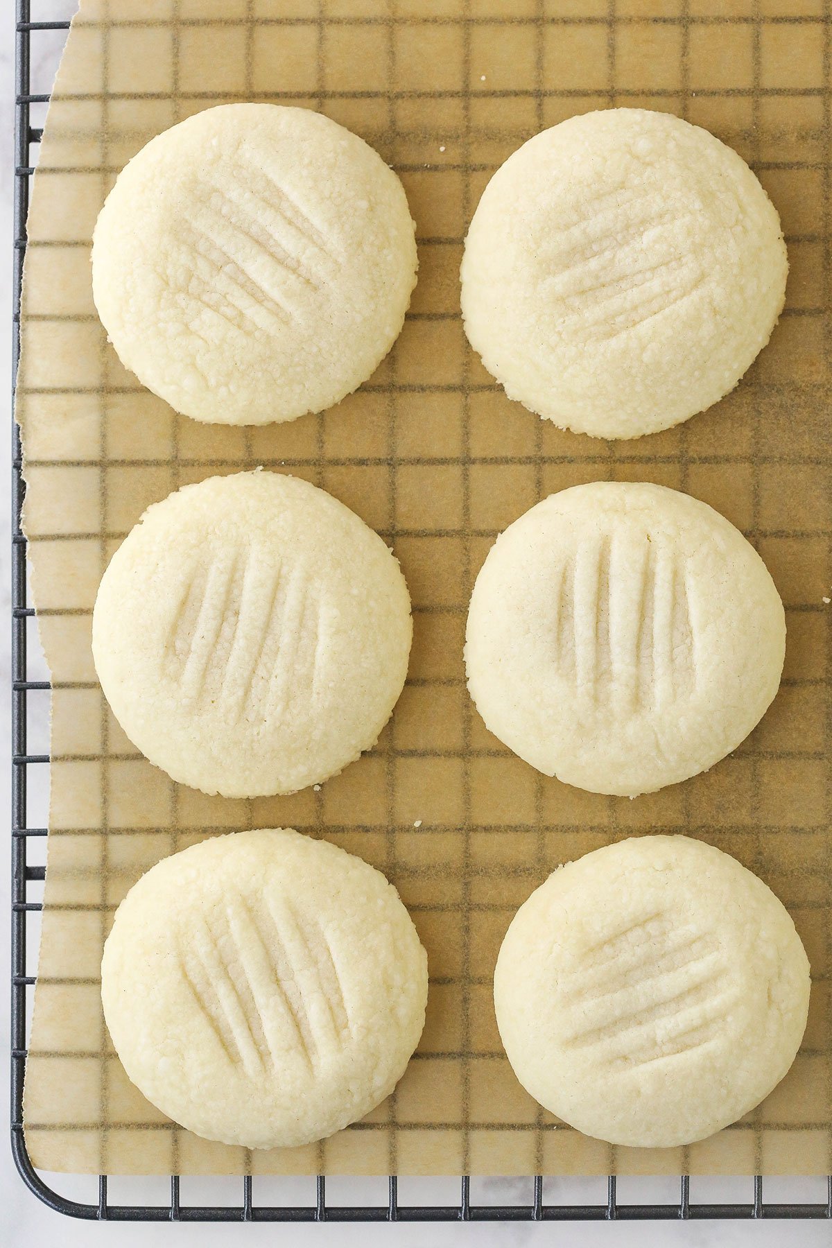 Six uncoated melting moments cookies on a cooling rack lined with parchment paper