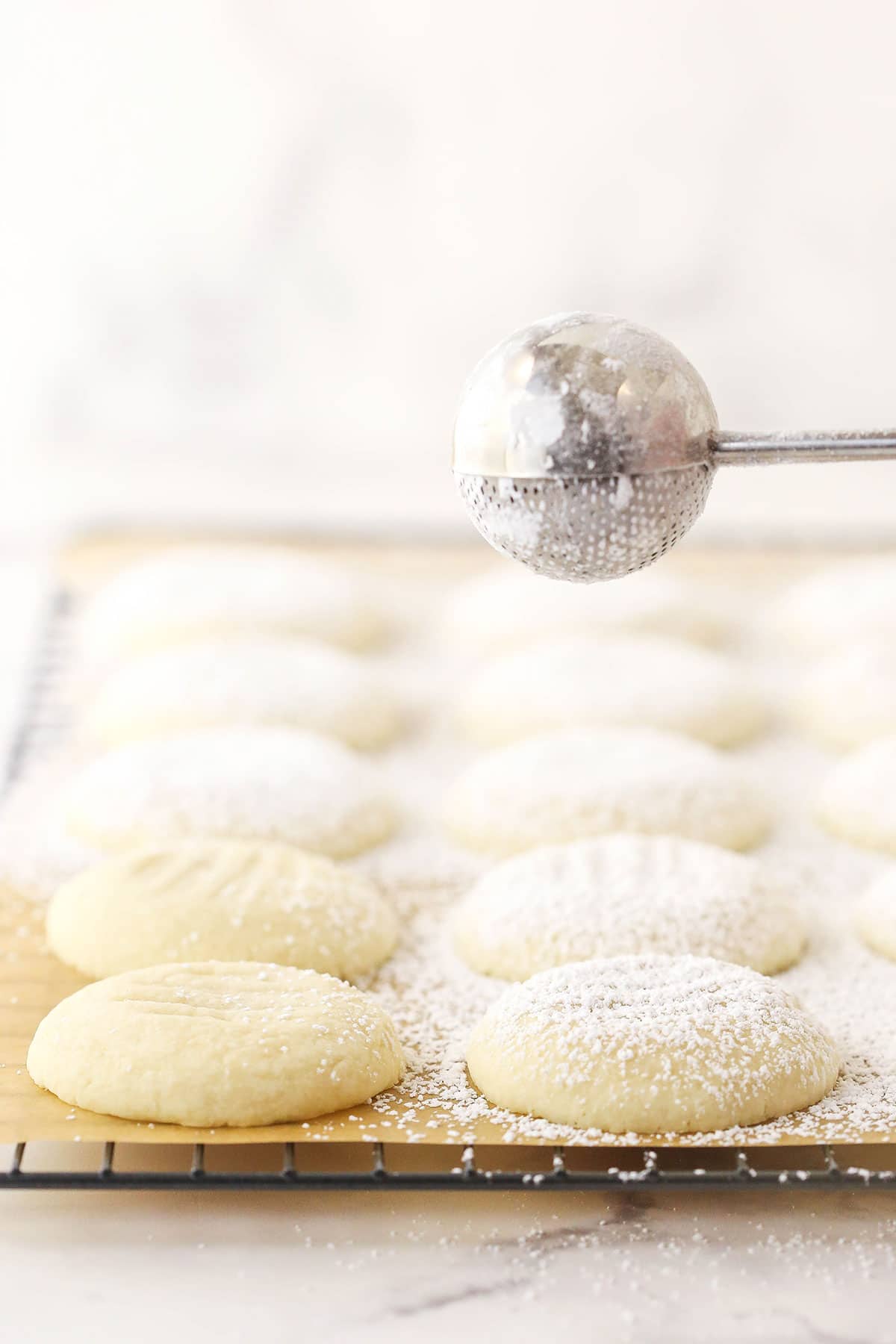 Powdered sugar being dusted over a batch of freshly-baked butter cookies.