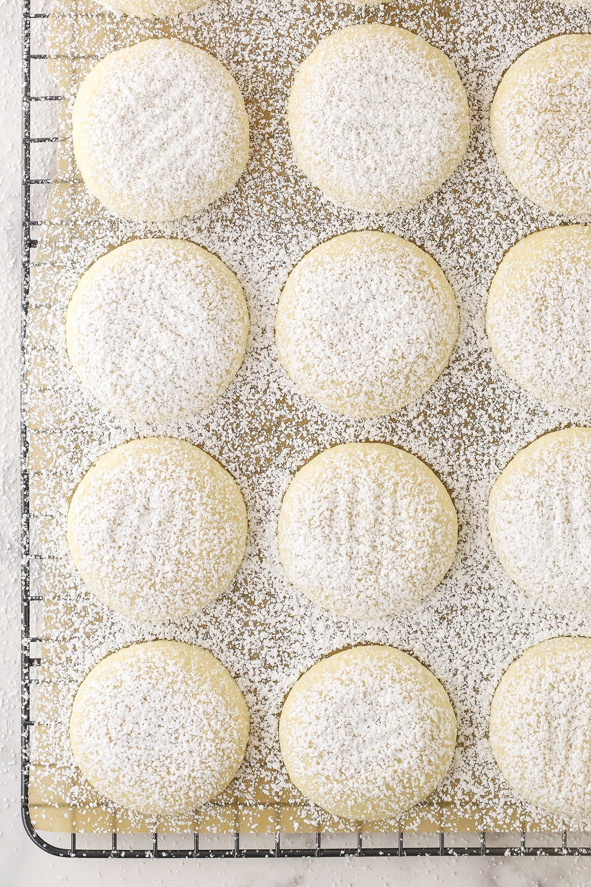 A bird's-eye view of a batch of vanilla butter cookies on a wire rack with a sheet of parchment paper underneath the cookies.