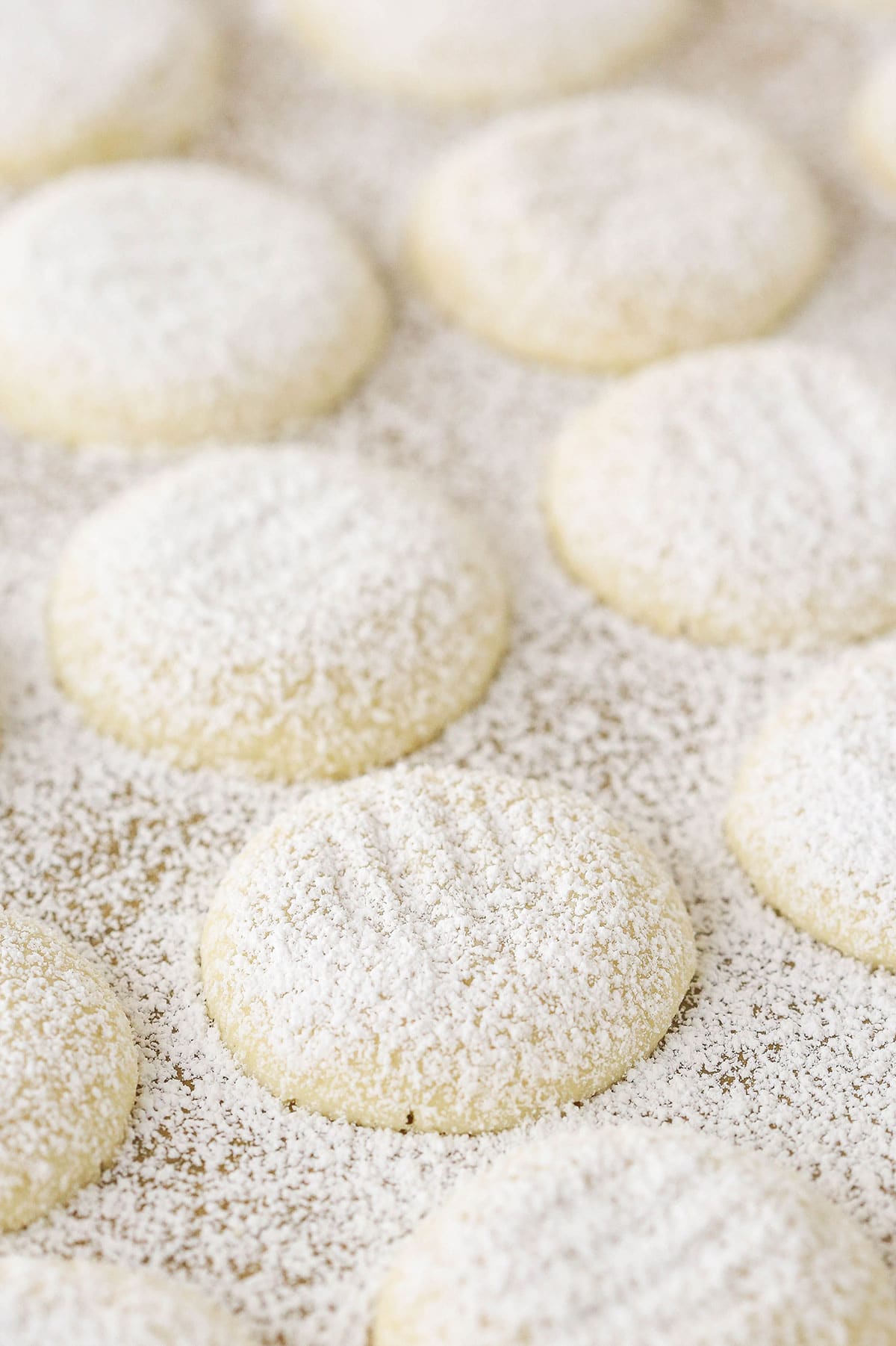 A bunch of butter cookies lined up on a smooth surface covered in powdered sugar.