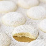 A uniform arrangement of powdered sugar coated vanilla butter cookies with one missing a bite