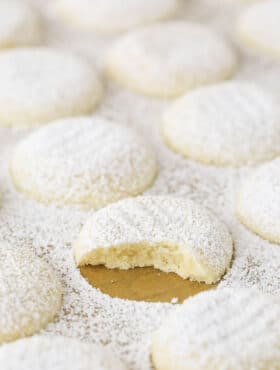 A uniform arrangement of powdered sugar coated vanilla butter cookies with one missing a bite