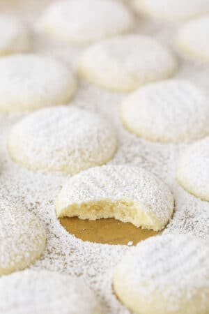 A uniform arrangement of powdered sugar coated vanilla butter cookies with one missing a bite