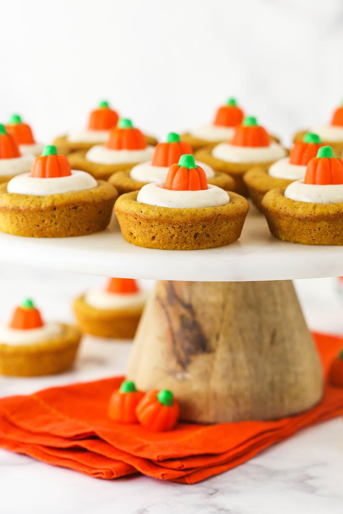 A large cake stand holding a batch of homemade pumpkin cookies with an orange cloth napkin underneath it