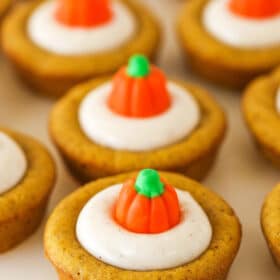 A close-up shot of pumpkin cheesecake cookie cups lined up on top of a smooth white surface