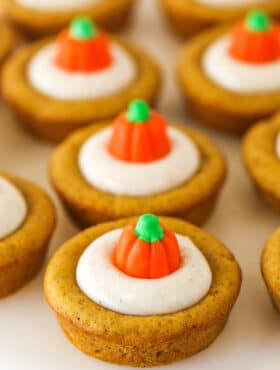 A close-up shot of pumpkin cheesecake cookie cups lined up on top of a smooth white surface