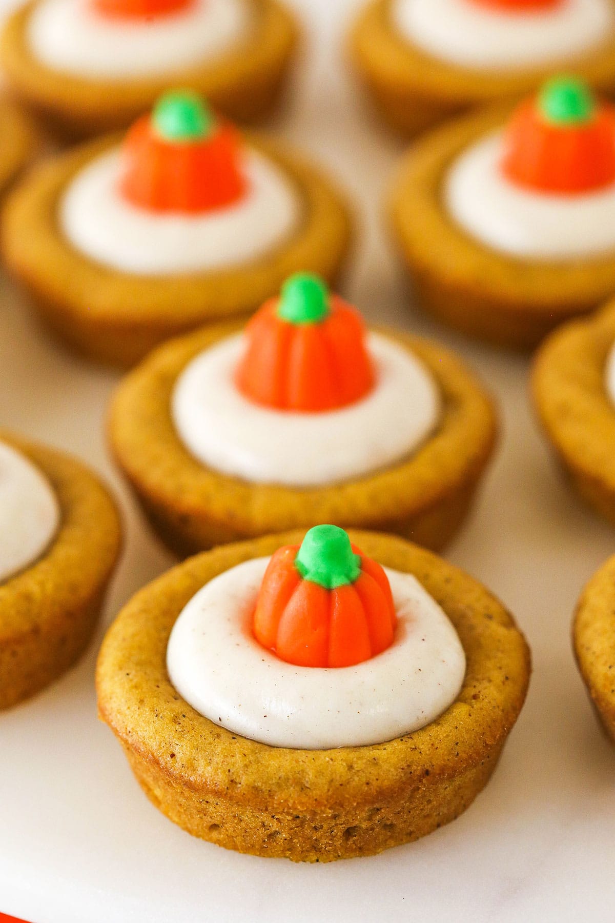 A close-up shot of pumpkin cheesecake cookie cups lined up on top of a smooth white surface