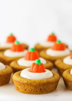 Pumpkin cookies lined up on a white surface with a candy pumpkin on top of each one