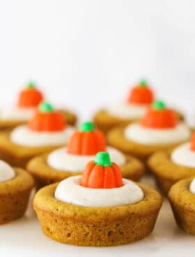 Pumpkin cookies lined up on a white surface with a candy pumpkin on top of each one
