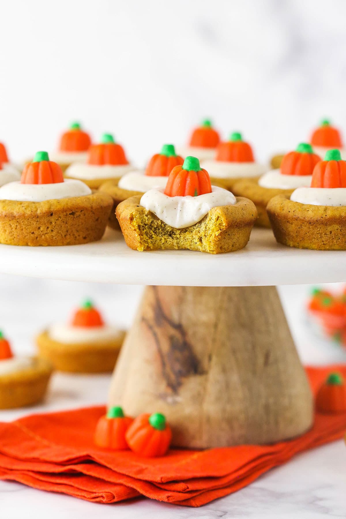 A bunch of pumpkin cheesecake cookie cups on a cake stand with one missing a bite