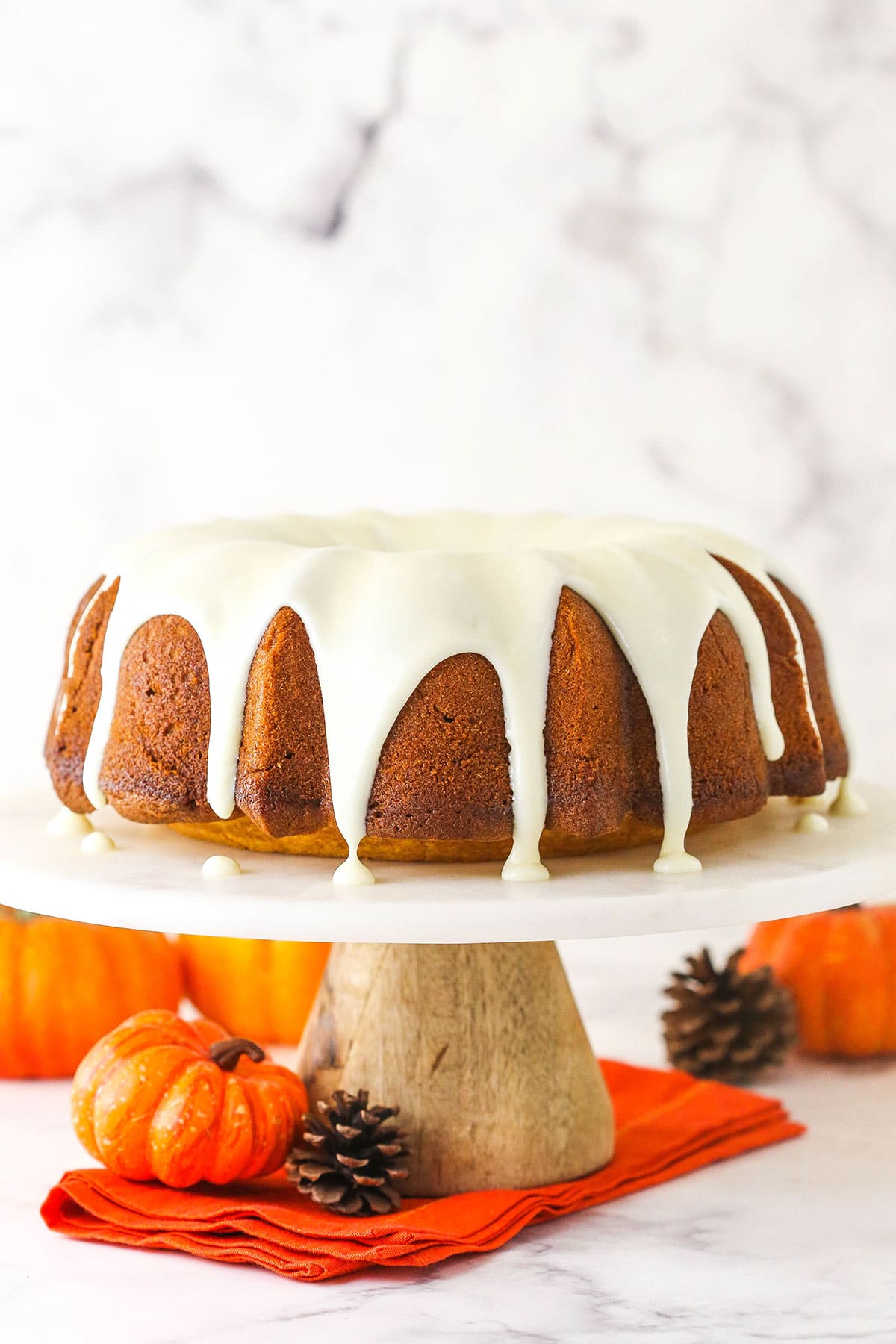 Pumpkin pound cake on marble and wood cake stand with orange cloth underneath.