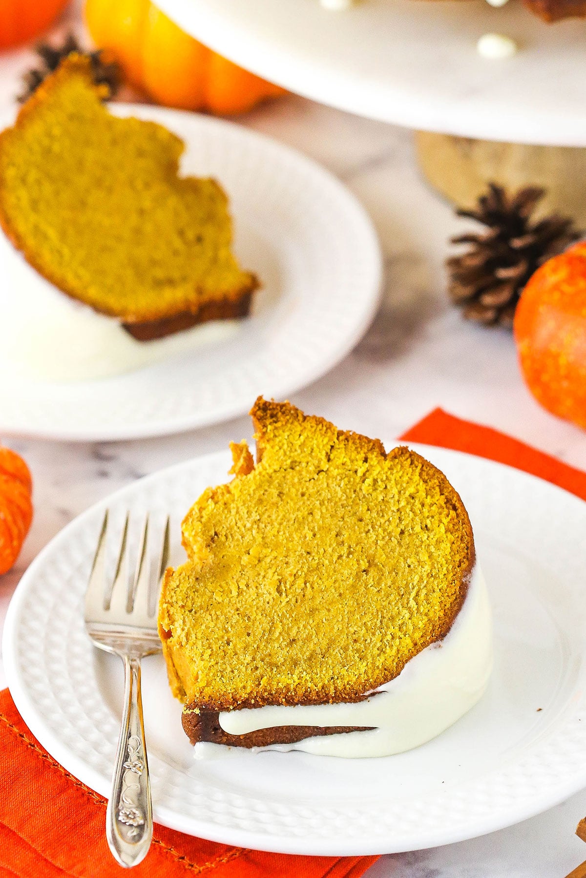 Pumpkin pound cake slice on white plate with orange napkin.