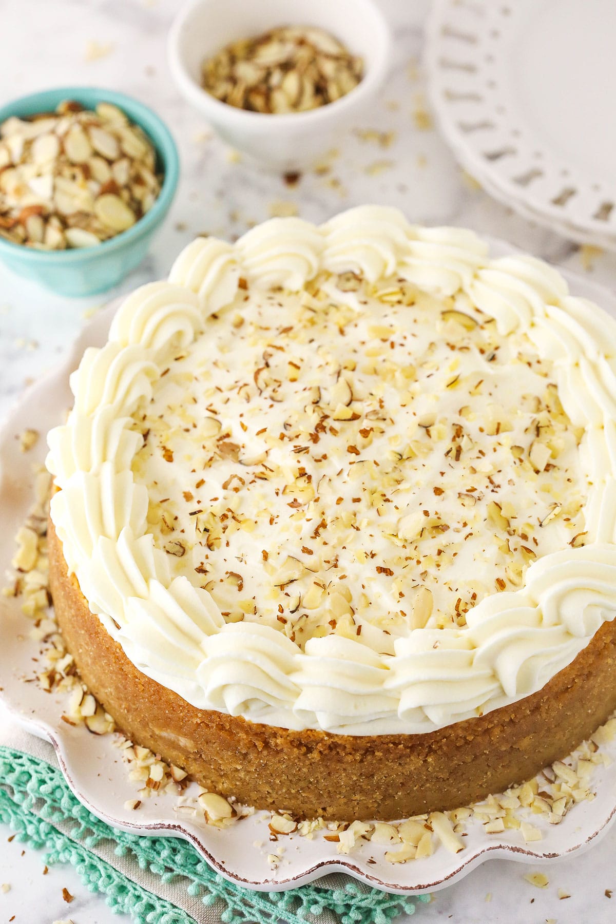 A whole Amaretto cheesecake on a cake stand with two dishes of almonds and two small plates in the background